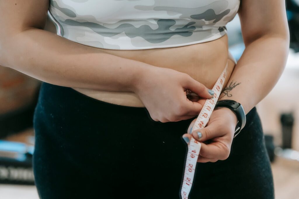 Mulher com sobrepeso e em roupas de academia mede a cintura com uma fita métrica