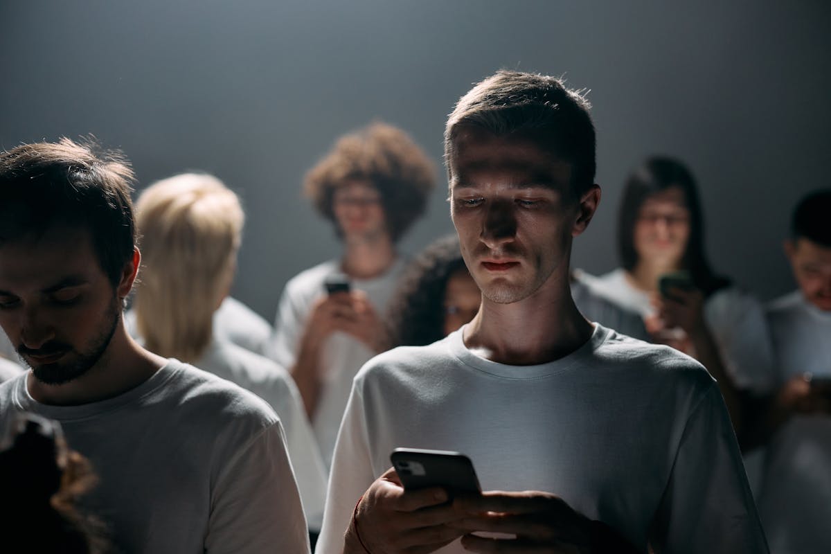 Jovens de camisa branca olhando para as telas de seus celulares com a cabeça baixa
